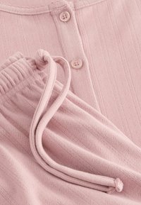 Tessuto rosa chiaro con texture a righe verticali, dotato di coulisse e due bottoni per la chiusura. Materiale morbido e accogliente.