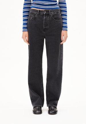 Jeans de mezclilla negra de pierna ancha con bolsillos frontales y cierre de botón y cremallera. Llevado con una blusa ajustada de rayas azul y blanca.