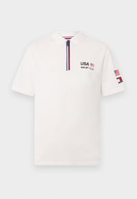Hvid polo skjorte med krave, lynlås lukning og korte ærmer. Har "USA" og "SAIL GP TEAM" broderet i sort med flag accenter.