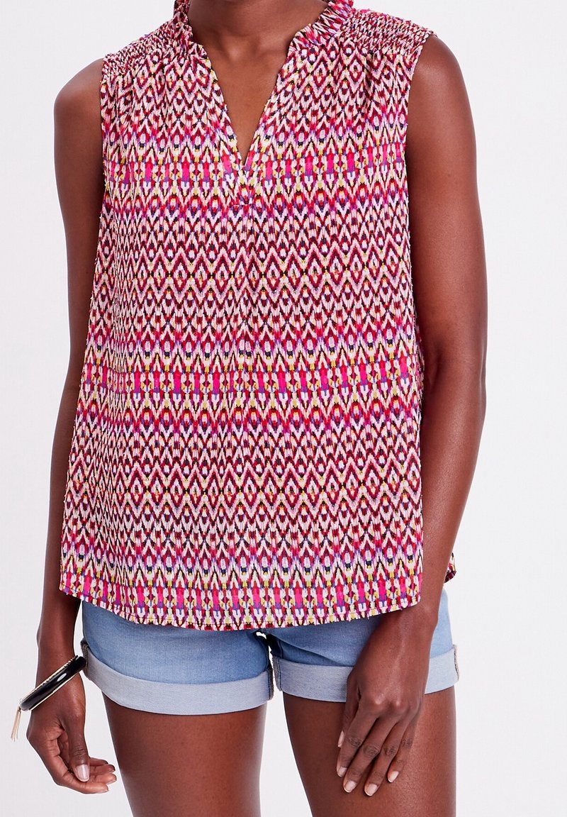 Haut sans manches rose avec un motif géométrique en rouge, blanc et vert. Col classique, tissu léger, design à longueur de hanches.