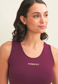 Top sin mangas burdeos con escote redondeado, que presenta un logo plateado "FREDDY" en el centro, fabricado en una tela suave y elástica.