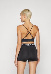 Sutian atlético preto com alças cruzadas e um tecido texturizado, combinado com calções ajustados pretos com uma faixa branca com a inscrição "PUMA".
