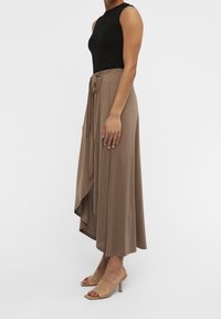 Haut sans manches noir à côtes associé à une longue jupe fluide taupe avec une taille à nouer, une texture douce et un ourlet asymétrique.
