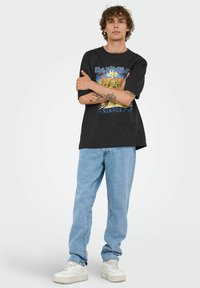 Sort bomulds T-shirt med Iron Maiden grafik i gule, blå og hvide detaljer. Sammen med lyseblå denim jeans og hvide sneakers.