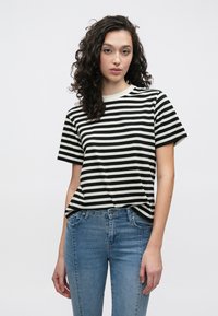 Črno-bela tanka majica s kratkimi rokavi in okroglim izrezom, kombinirana s svetlo modrimi kavbojkami. Mehka tkanina in sproščen kroj.