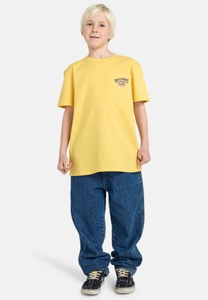 Geel katoenen t-shirt met een ronde hals en korte mouwen, voorzien van een paarse grafische print, gecombineerd met ruime blauwe denim jeans.