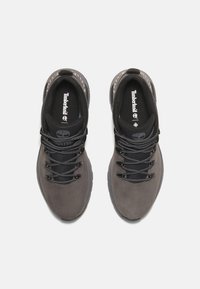 Zapatos de senderismo de color gris oscuro con una parte superior de cuero suave, cordones negros, cuello acolchado y una suela de goma texturizada. Logo de Timberland en la lengüeta.