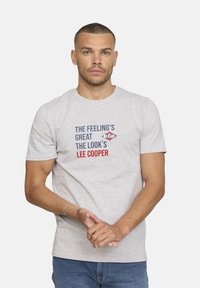 T-shirt en coton gris à manches courtes, avec un texte bleu et rouge : "LA SENSATION EST GÉNIALE, LE LOOK EST LEE COOPER." Design simple à col rond.