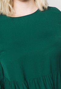 Vestito verde acqua a maniche corte con scollatura rotonda e orlo inferiore arricciato. Tessuto dalla texture liscia con una leggera lucentezza.