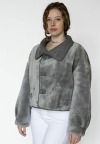 Harmaa tekoturkistakki, jossa on suuri kauluskäänne, napitus ja leveät hihat. Takissa on pehmeä tekstuuri ja hienovarainen värivaihtelu.