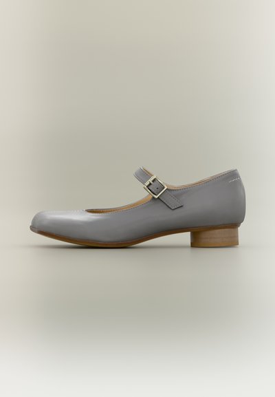 Chaussure Mary Jane en cuir gris avec une bride unique à boucle et un petit talon en bois empilé sur fond neutre.