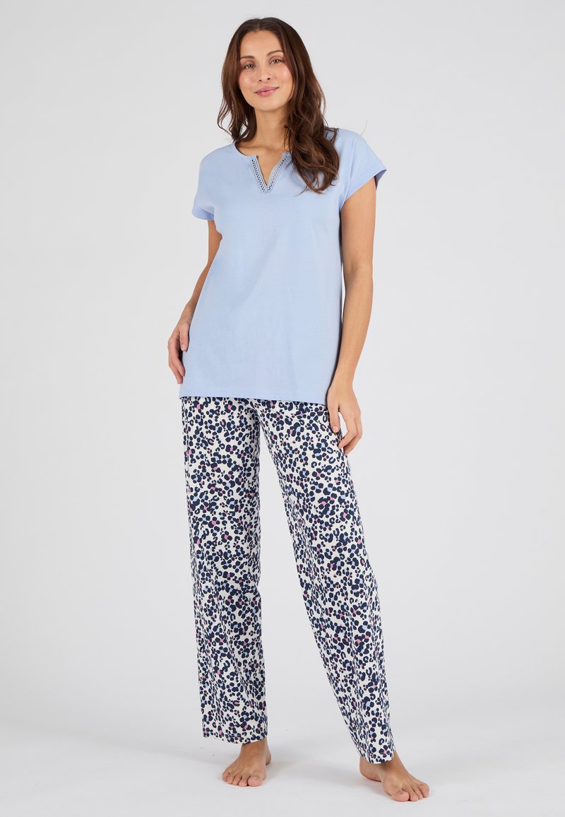 Top corto de manga corta azul claro con escote en V y adornos decorativos; combinado con pantalones holgados blancos con un patrón de manchas azules y moradas.