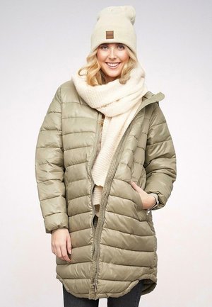 Giacca imbottita verde oliva con trapuntatura orizzontale, zip frontale e tasche laterali, abbinata a una sciarpa crema e un cappellino lavorato a maglia.