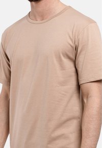 Vaaleanbeige puuvillapaita, lyhyet hihat, pyöreä kaula-aukko, sileä rakenne, hieman joustava, minimalistinen muotoilu, ei näkyviä kuvioita tai logoja.