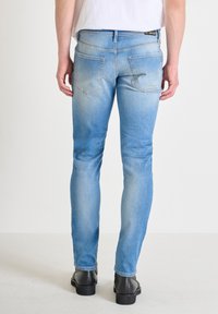 Jeans de mezclilla azul de corte ajustado con un aspecto desgastado, bolsillos delanteros y traseros, y una cintura estándar, combinados con zapatos negros.