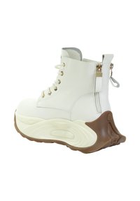Białe skórzane buty z złotymi oczkami, bocznymi zamkami błyskawicznymi i masywną brązową podeszwą. Unikalny konturowany wzór podeszwy dodaje wizualnego uroku.