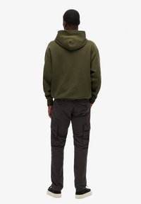 Sweatshirt à capuche vert olive avec une coupe ample, associé à un pantalon cargo gris foncé doté de plusieurs poches, et des baskets noires.