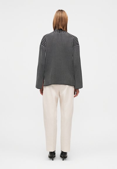 Μαύρο και λευκό ριγέ σακάκι με μακριά μανίκια, υφασμάτινη υφή και στρογγυλή λαιμόκοψη, σε συνδυασμό με κρεμ παντελόνι με στενή γραμμή και μαύρα τακούνια.