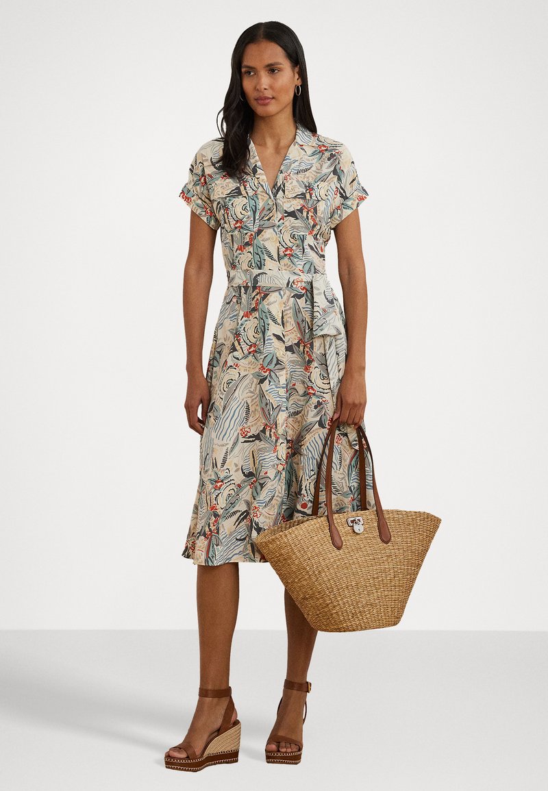 Sukienka w kwiatowy wzór z lekkiego materiału, z krótkimi rękawami i paskiem w talii. Połączona z plecioną torbą ze słomy i brązowymi sandałami na platformie.