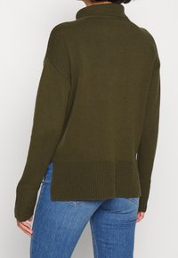 Maglione a collo alto in verde oliva, con spalle scese, polsini a coste e spacchi laterali sull'orlo per un tocco di originalità.