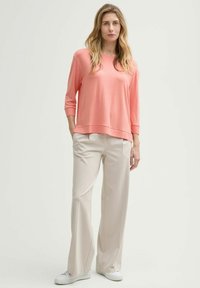 Top in morbido tessuto rosa chiaro con maniche a 3/4, abbinato a pantaloni larghi crema e sneakers bianche; vestibilità casual e rilassata.