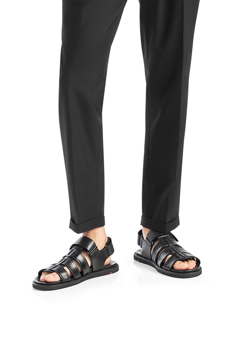 Sandali in pelle nera con più cinturini, design aperto alla punta e suola piatta, abbinati a pantaloni cropped neri.