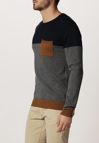 Mäns tröja i marinblått, grått och brunt. Har rundad halsringning, långa ärmar och en bröstficka. Ribbstickade ärmslut och nederkant ger textur.