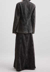 Set di giacca e gonna in denim grigio scuro con cuciture a vista. La giacca presenta un colletto a punta, mentre la gonna ha un design lungo e fluido.