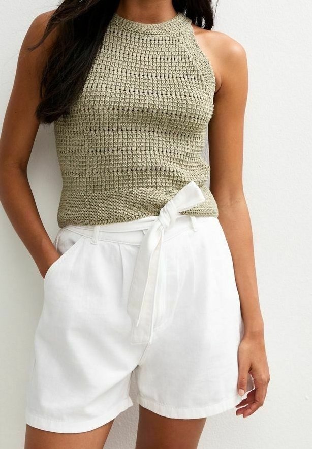 Top de tirantes de ganchillo en verde oliva claro con un cuello alto, combinado con pantalones cortos de lino blancos que tienen un detalle de lazo en la parte delantera y bolsillos laterales.