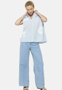 Camicia a righe blu e bianche con ricami floreali, maniche corte e vestibilità rilassata, abbinata a jeans a gamba larga di un blu chiaro.