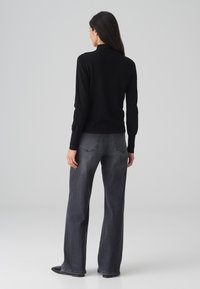 Schwarzes Langarmoberteil mit einem Rüschensaum, kombiniert mit dunkelgrauen weiten Jeans, die über Gesäßtaschen und subtile Nähte verfügen.