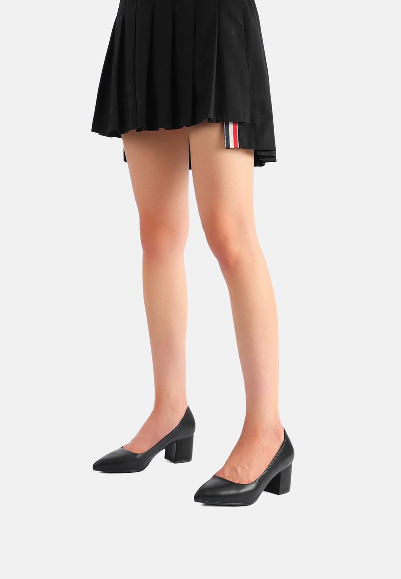 Scarpe in pelle nera con tacco a blocco e punta affusolata. Texture liscia, stile minimalista, adatte per un abbigliamento formale o casual.