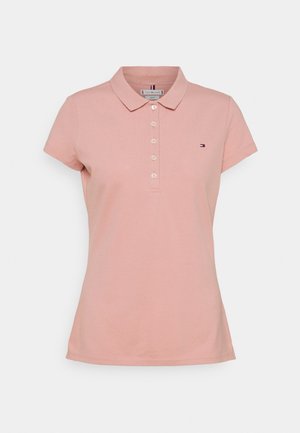 Naisten vaaleanpunainen lyhythihainen poolopaita, jossa on napillinen kaulus ja vasemmassa rinnassa pieni kirjailtu logo.