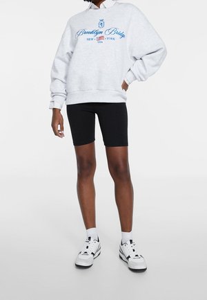 Gray sweatshirt with blue "Brooklyn Bridge" text, black bicycle shorts, and white sneakers, featured against a plain background.