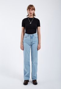 Top negro de manga corta, jeans de pierna recta de talle alto en azul claro y calzado grueso marrón oscuro. Diseño simple, tejido suave, sin patrones.