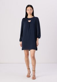 Vestido azul-marinho, até ao joelho, com mangas longas e bufantes e um detalhe em forma de olho de fechadura na gola, feito de tecido leve. Textura suave.