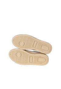 Suole di scarpe di colore chiaro con un motivo testurizzato, caratterizzate da accenti circolari e rettangolari, e un logo a cuore in rilievo sulla parte inferiore.