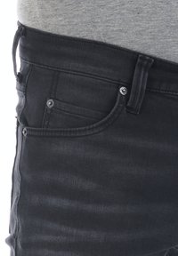 Jeans in denim nero con un design aderente, stile a cinque tasche e delicate sfumature. Presentano dettagli in metallo per i bottoni e cuciture in tono.