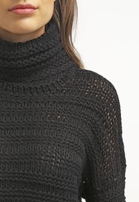 Maglione a collo alto nero a maglia, con una lavorazione tessuta ampia e morbida. Presenta un colletto oversize e linee strutturate, creando una vestibilità rilassata.
