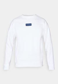 Sweat-shirt blanc en coton, avec une étiquette bleue rectangulaire portant les inscriptions "PARIS" et "SAINT-GERMAIN" sur le devant. Coupe décontractée, encolure ras du cou.