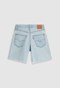 Svetlo modri denim kratke hlače z neobdelanim spodnjim robom, ki imajo zadnje žepe in rjavo usnjeno etiketo na pasu, ki prikazuje klasične dizajnerske elemente Levi's.