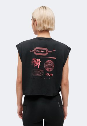 Osoba z krótkimi blond włosami, ubrana w czarny bezrękawnik z czerwonym tekstem graficznym i abstrakcyjnymi wzorami na plecach.