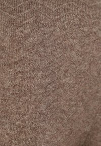 Bruin gebreid stof met een vissengraatpatroon, voorzien van een zachte textuur en subtiele variaties in tint over het oppervlak.