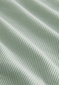 Närbild av mjukt, grönt texturerat tyg med horisontella ribbade linjer, som visar ett slätt, skönt vågmönster.