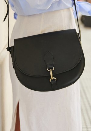 Czarna skórzana torba na ramię z zakrzywioną klapą, złotymi ozdobami i regulowanym paskiem. Gładka faktura i przeszycia.