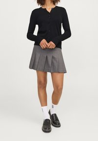 Svart knapp-up cardigan med rund halsringning, ihop med en grå veckad minikjol. Svarta loafers och vita ankelsockor fulländar looken.