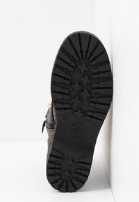 Semelle de bottine noire avec des crampons profonds, motifs floraux et géométriques, et fermeture éclair latérale visible sur fond blanc.