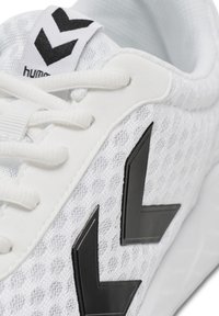 Scarpa atletica bianca con tomaia in rete traspirante, design a chevron nero come accento, lacci e suola testurizzata per aderenza.