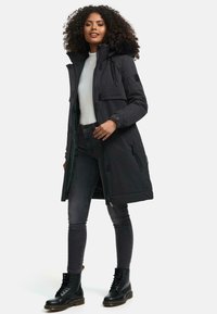 Black parka with a fur-lined hood, front zip closure, two side pockets, and a regular fit. Paired with gray jeans and black lace-up boots.