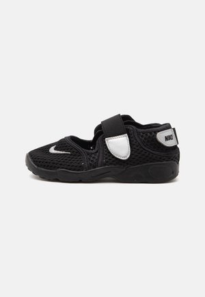 Sort Nike mesh sneaker med en bred velcrorem og hvide logoplapper på siden og hælen.